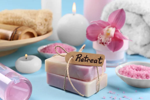 Retreat concept. Composition with card, different spa products and burning candles on light blue background, closeup