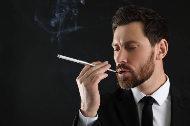 Siyah arkaplanda sigara içmek için uzun sigara tutacağı, metin için boşluk kullanan adam