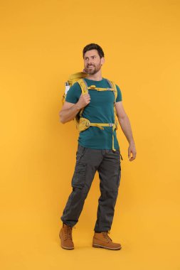 Turuncu arka planda sırt çantalı mutlu bir adam. Etkin turizm