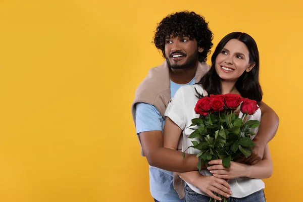 International dating. Happy couple with bouquet of roses on yellow background, space for text