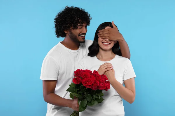 International dating. Handsome man presenting roses to his beloved woman on light blue background