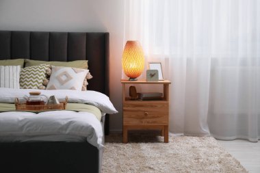 Konforlu yatak, lamba ve odasındaki ahşap komodinin üzerindeki farklı dekorlarla dolu bir sepet. Şık iç mekan