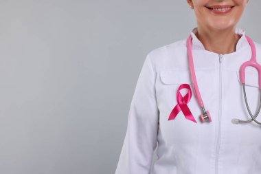 Açık gri arka planda pembe kurdeleli ve steteskoplu bir doktor, yakın plan ve metin için boşluk. Göğüs kanseri farkındalığı