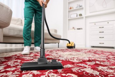 Kuru temizlemeci çalışanı halı süpürüyor, elektrikli süpürgeyle kapalı alanda, yakın plan. Metin için boşluk