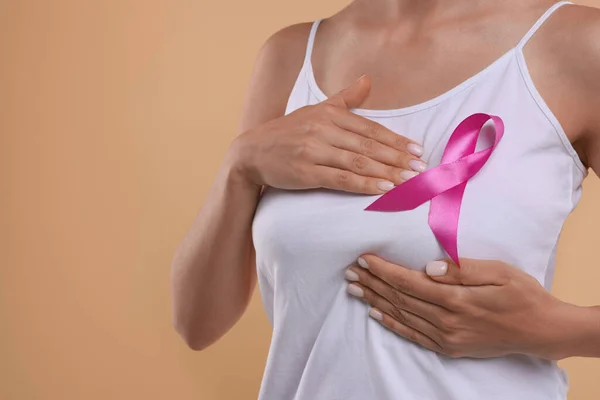 Breast cancer awareness. Woman with pink ribbon doing self-examination on light brown background, closeup. Space for text