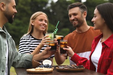 Mutlu arkadaşlar bardaklarını dışarıda kokteyllerle tokuşturuyorlar.