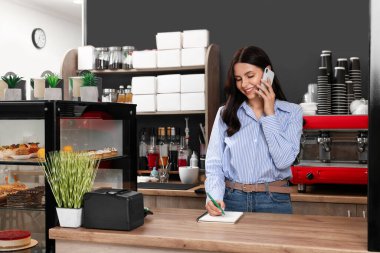 Dükkan sahibi kafede vitrinde çalışırken telefonla konuşuyor.