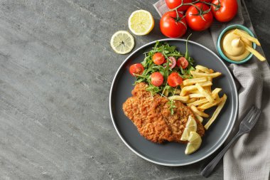 Patates kızartması, domates ve roka ile servis edilen lezzetli şnitzeller gri masada, düz konumda. Metin için boşluk