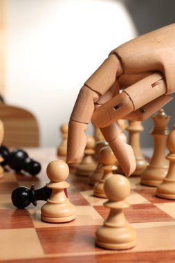 Robot satranç taşını hareket ettiriyor, yakın plan. Tahta el, yapay zekayı temsil ediyor.