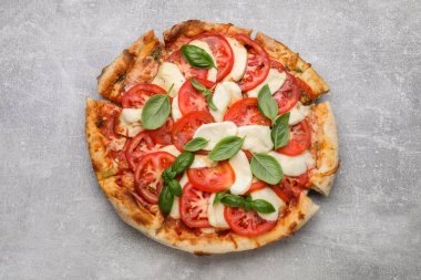 Domatesli lezzetli Caprese pizzası, mozzarella ve açık gri masada fesleğen.