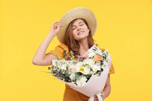 黄色の背景に美しい花の花束とわら帽子で幸せな女性 — ストック写真
