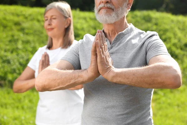 Üst düzey çift dışarıda yoga yapıyor, seçici bir odak noktası var.