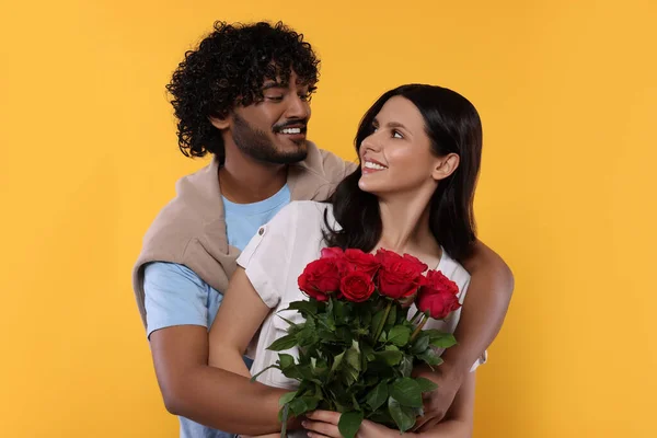 International dating. Happy couple with bouquet of roses on yellow background
