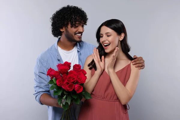 International dating. Handsome man presenting roses to his beloved woman on light grey background