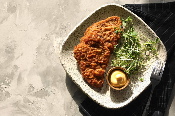 Tasty schnitzels served with sauce and microgreens on grey textured table, top view. Space for text