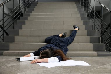 Merdivenlerden düştükten sonra yerde yatan dağınık klasörlü baygın bir kadın.