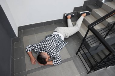 Bilinçsiz bir adam merdivenlerden düştükten sonra yerde yatıyor.