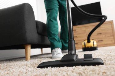 Kuru temizlemeci çalışanı halı süpürüyor, elektrikli süpürge içeride, yakın plan.