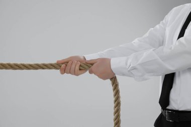 Tartışma konsepti. İş adamı açık gri arka planda ip çekiyor, yakın plan.
