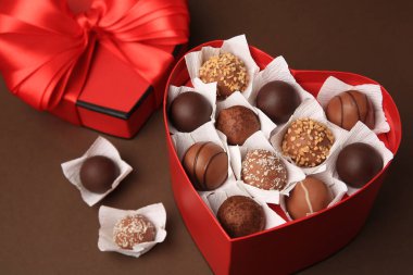 Kahverengi arka planda lezzetli çikolata şekerleri olan kalp şeklinde bir kutu, yakın plan.