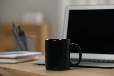 İş yerindeki ahşap masada siyah seramik bardak ve laptop.