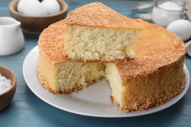 Lezzetli sünger keki ve açık mavi ahşap masa malzemeleri, yakın plan.