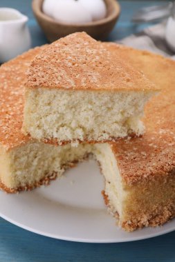 Açık mavi ahşap masada kesilmiş lezzetli sünger keki, yakın plan.