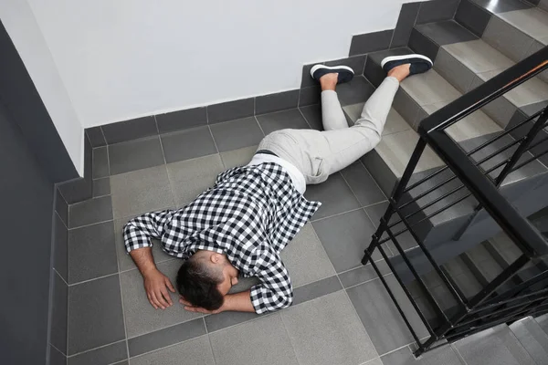 Unconscious man lying on floor after falling down stairs indoors, above view