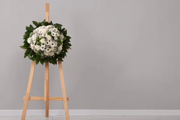花环放在靠近灰色墙壁的木制壁上 放在室内举行葬礼 案文的篇幅 — 图库照片