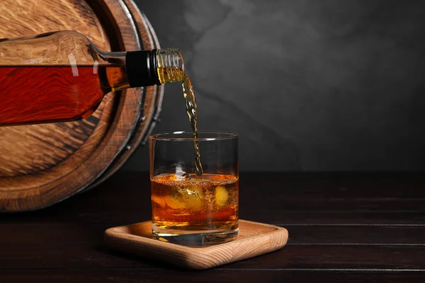 Wlewanie Whisky Butelki Szklanki Kostkami Lodu Pobliżu Drewnianej Beczki Stole — Zdjęcie stockowe