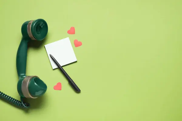 Long-distance relationship concept. Telephone receiver, empty note, paper hearts and pen on light green background, flat lay with space for text