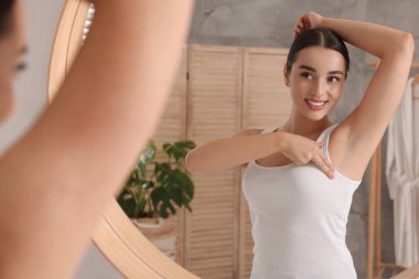 Güzel genç bir kadın banyoda aynanın yanında göğüslerini muayene ediyor.