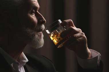 Takım elbiseli adam kahverengi arka planda viski içiyor.