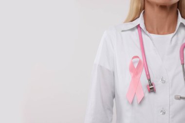 Beyaz arka planda pembe kurdeleli ve steteskoplu bir doktor, yakın plan ve mesaj için boşluk. Göğüs kanseri farkındalığı
