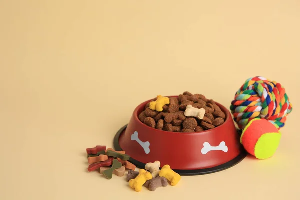 Dry pet food in bowl, vitamins and toys on beige background, space for text