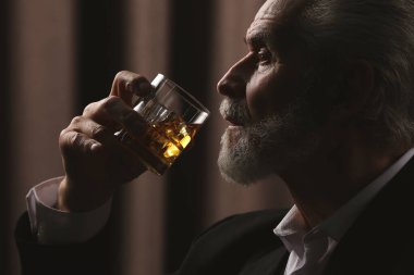 Takım elbiseli adam kahverengi arka planda viski içiyor.