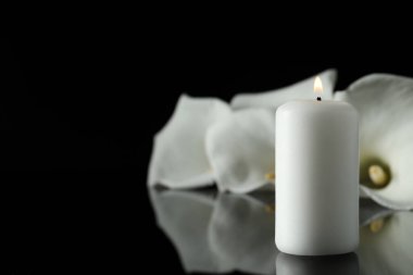 Karanlıkta siyah ayna yüzeyinde yanan mum ve beyaz zambak çiçekleri, metin için yeri olan yakın plan. Cenaze sembolü