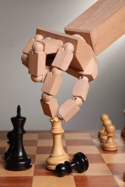 Robot satranç taşını açık gri arka plana doğru hareket ettiriyor, yakın plan. Tahta el, yapay zekayı temsil ediyor.