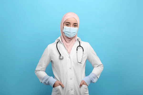 身穿头巾 医疗制服和浅蓝色背景防护面具的穆斯林妇女 — 图库照片