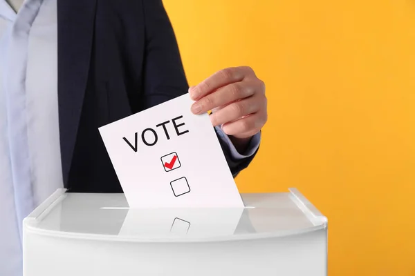 イエローバックグラウンドで投票ボックスに紙を貼り付けた女性 — ストック写真