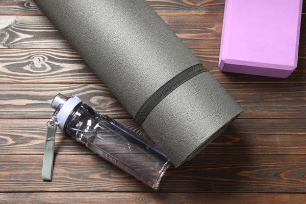 Exercise mat, yoga block and bottle of water on wooden floor, flat lay