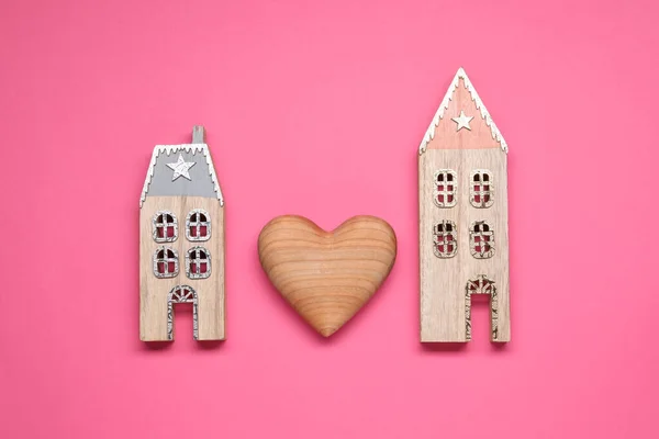 Long-distance relationship concept. Decorative heart between two house models on pink background, flat lay
