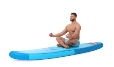 Beyaz arka planda mavi SUP tahtasında yoga yapan yakışıklı bir adam.