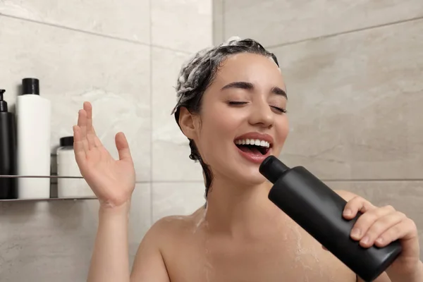 Washing hair. Happy woman with bottle singing in shower