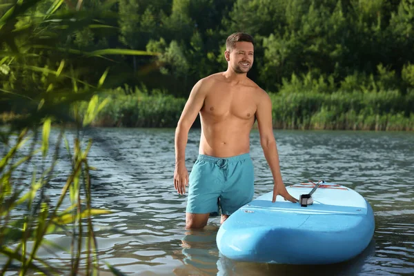 Man standing near SUP board in river water on sunny day