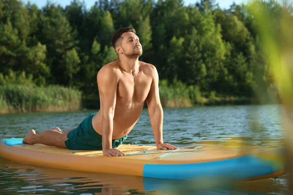 男人在河边的彩色Sup板上练习瑜伽 — 图库照片