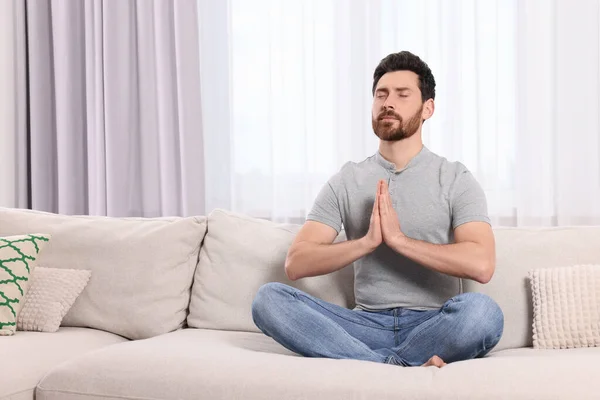 Man meditating on sofa at home, space for text