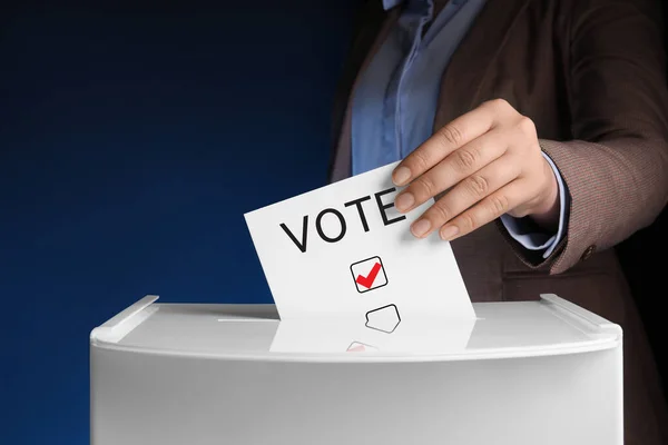 ダークブルーの背景に投票ボックスに紙を貼る女性 — ストック写真