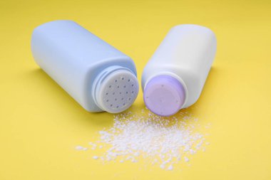 Sarı arka planda şişeler ve dağınık toz tozu, yakın plan. Bebek kozmetik ürünleri