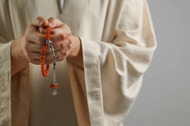 Misbaha 'lı Müslüman bir adam açık gri arka planda dua ediyor, yakın plan. Metin için boşluk